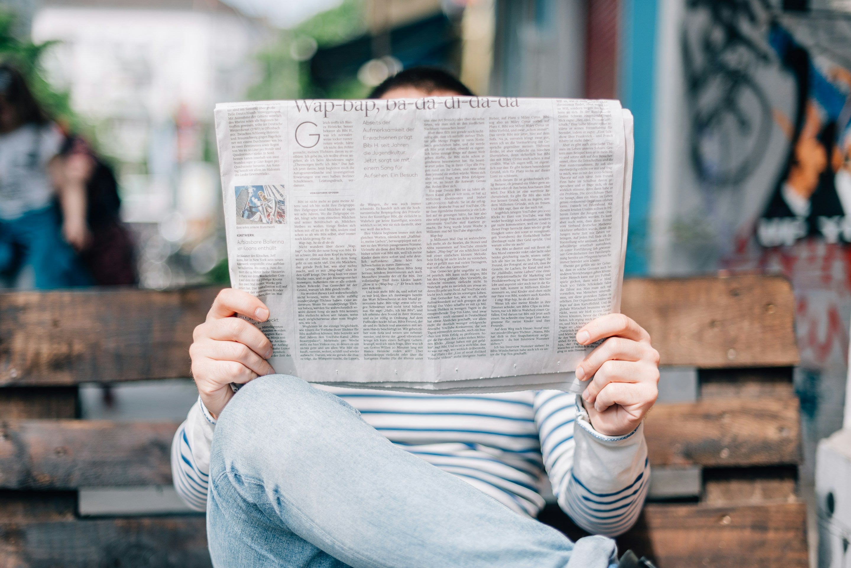 Person sitting on a bench reading a newspaper in an urban setting